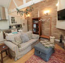 A living room with a striped sofa a wooden stool an ottoman and a kitchen area at The Forge Nr.Seahouses