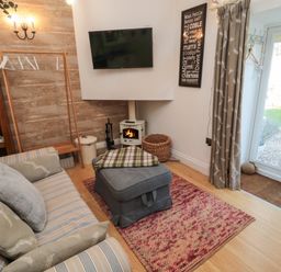 A living room with a striped sofa, ottoman, fireplace, mounted TV, and glass doors at The Forge in Nr Seabouses