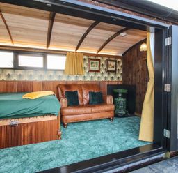 An interior room with a brown leather sofa a green carpet a bed with green bedding and yellow curtains at GWR Wagon - Victoria Station Ludlow