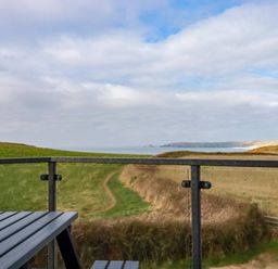 A view of a coastal path and grassy fields from a balcony with a wooden table at Jacana in Perranporth