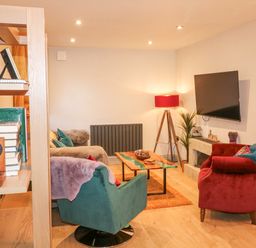 A living room with armchairs a coffee table a TV on the wall and a bookshelf at Orchard Retreat Staycation in Kirton