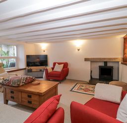 A living room with red armchairs a wooden coffee table a wood stove and a television at Springfield in Kingsand