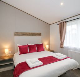 A bedroom with a double bed red cushions bedside tables lamps and window with curtains at Peony in Eardisland