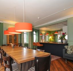 A dining area with a long wooden table and chairs under orange pendant lights next to a bar counter and sofa at Sycamore Apartment in Lifton