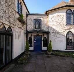 An exterior courtyard with a blue door flanked by two planters and a building with arched windows at Sycamore Apartment in Lifton