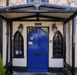 An entrance with a blue arched door and two arched windows with black frames at Sycamore Apartment in Lifton