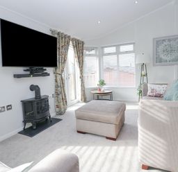 A living room with a wall-mounted TV stove beige sofas and a round side table at Swifts Reach Lodge Kirkstone 10 Limefitt Park near Windermere