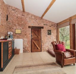 A room with a leather armchair a wooden sideboard and a wooden door with stone walls and large windows showing a garden at The Barn in Spaxton