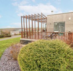 A wooden house with a pergola on the deck and shrubs in the garden at Hepworth in Portreath