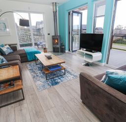 A living room with brown sofas and blue cushions a wooden coffee table wood burner and a television at Hepworth in Portreath