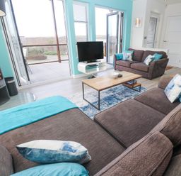 A living room with two brown sofas pillows a wooden coffee table a television a fireplace and an open door to a deck at Hepworth in Portreath