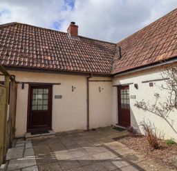 An outdoor courtyard with two doors labeled Garden Cottage and Meadow Cottage with tiled roofs and some plants at Garden Cottage in Upottery