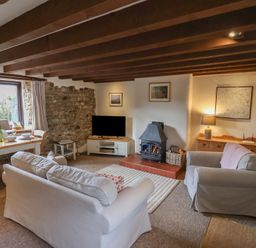 A living room with two sofas a wood-burning stove a dining table and chairs at Garden Cottage in Upottery