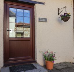 A wooden door with window panes and a hanging basket of flowers with a potted plant below at Garden Cottage in Upottery