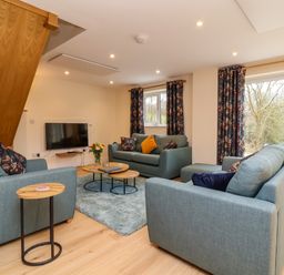 A living room with blue sofas a wall mounted TV round wooden tables and floral curtains at Hideaway in Great Torrington