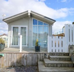 Front view of a small wooden house with glass doors and windows on a raised deck with wooden steps and white fencing Ocean Breeze Abersoch