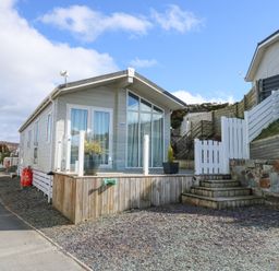 A small modern house with large windows and a wooden deck with potted plants at Ocean Breeze in Abersoch