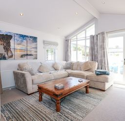 A living room with a beige sectional sofa wooden coffee table and large windows at Ocean Breeze in Abersoch