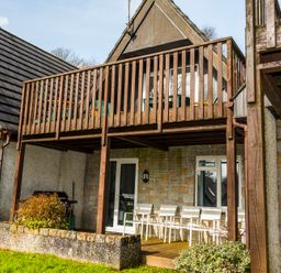 An outdoor patio area with white chairs under a wooden balcony attached to a stone house at Valley Lodge 37 in St Anns Chapel Cornwall
