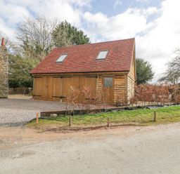 A wooden garage with two skylights next to a gravel driveway and a stone chimney at Pheasants Rise Apartment in Ross-On-Wye