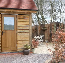 An outdoor area with a wooden door on a timber building a small white table with two chairs and potted plants at Pheasants Rise Apartment in Ross-On-Wye