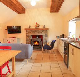 A living room with a fireplace and kitchen area at Shane's Cottage in Falcarragh, County Donegal