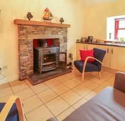 A living room with a fireplace and kitchen area at Shane's Cottage in Falcarragh, County Donegal