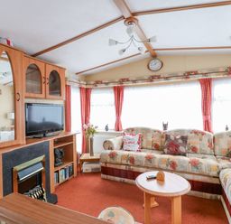 A living room with a floral sofa a wooden cabinet with a television and a fireplace at 120 Caravan in Hemsby