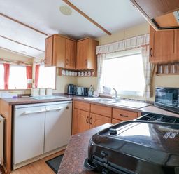 A kitchen area with wooden cabinets a sink a microwave and an appliance on the counter at 120 Caravan in Hemsby