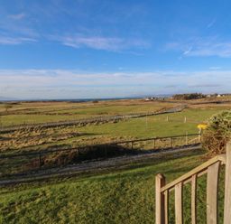 A grassy field with a wooden fence and steps leading down at Creag Mhor Lodge Back of Keppoch near Arisaig
