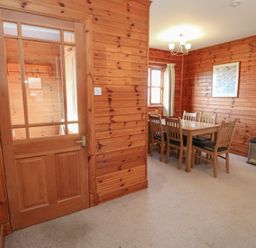 A dining area with a wooden table and six chairs near a window in a room with wooden walls at Creag Mhor Lodge Back of Keppoch near Arisaig