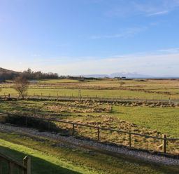 A rural landscape with fields fences a road and distant buildings at Glen Mhor Lodge in Arisaig