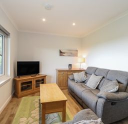 A living room with a gray sofa wooden coffee table TV on wooden stand and a window at Glen Mhor Lodge in Arisaig