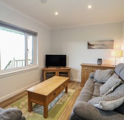 A living room with grey sofas a wooden coffee table a TV on a wooden stand and a sideboard with a lamp at Glen Mhor Lodge in Arisaig