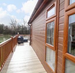A wooden deck with railing and seating area overlooking a lake at The Lake House in Marston near Barkston