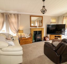 A living room with a cream sofa brown armchair fireplace and a large television at The Lake House in Marston near Barkston