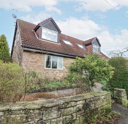 A stone house with a tiled roof and dormer windows surrounded by a garden and stone wall at Kerangarth in Corbridge