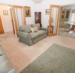 A living room with two sofas and a green rug opening into a dining area with a table and chairs at Kerangarth in Corbridge