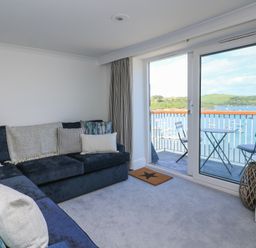 A living room with a sofa and sliding door leading to a balcony at 43 The Salcombe in Salcombe