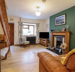 A living room with a brown leather sofa a green accent wall with a fireplace and a television on a wooden stand at Gwynfa in Ysbyty Ifan