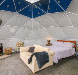 A dome-shaped room with a bed, sofa, wood burning stove, and a small chair at Meadow View - Bryn-Mawr Retreat in Brynmawr near Llanymynech