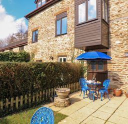 An outdoor patio with a blue table and chairs under a blue umbrella next to a stone house at Millers Loft in Modbury
