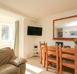 A dining area with a wooden table and chairs a wall-mounted television and a leather armchair at Millers Loft in Modbury