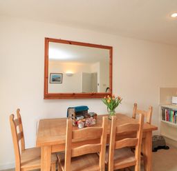A dining area with a wooden table and chairs a large mirror on the wall books and appliances on a kitchen counter at Millers Loft in Modbury