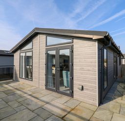 Exterior view of a single-story building with patio doors and windows on a paved patio at Number 43 The Poplars in Burnham Market