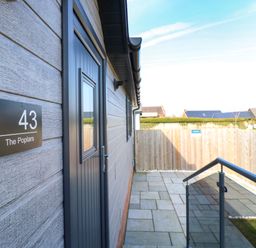An outdoor patio area with a dark door and a sign reading 43 The Poplars next to a wooden fence and stone tiles at Number 43 The Poplars in Burnham Market