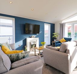A living room with sofas a TV on a blue wall and sliding doors at Number 43 The Poplars in Burnham Market