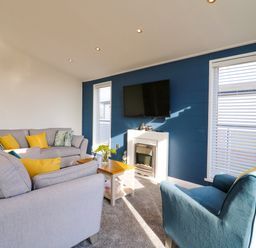 A living room with blue and gray sofas a coffee table and a wall-mounted TV at Number 43 The Poplars in Burnham Market