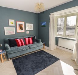 A living room with a green sofa red and black cushions a blue rug and framed pictures on the wall at 2 Summers Way in Moreton-In-Marsh