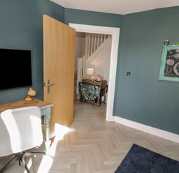 A room with a wooden desk chair tv mounted on wall and open door showing a hallway at 2 Summers Way in Moreton-In-Marsh